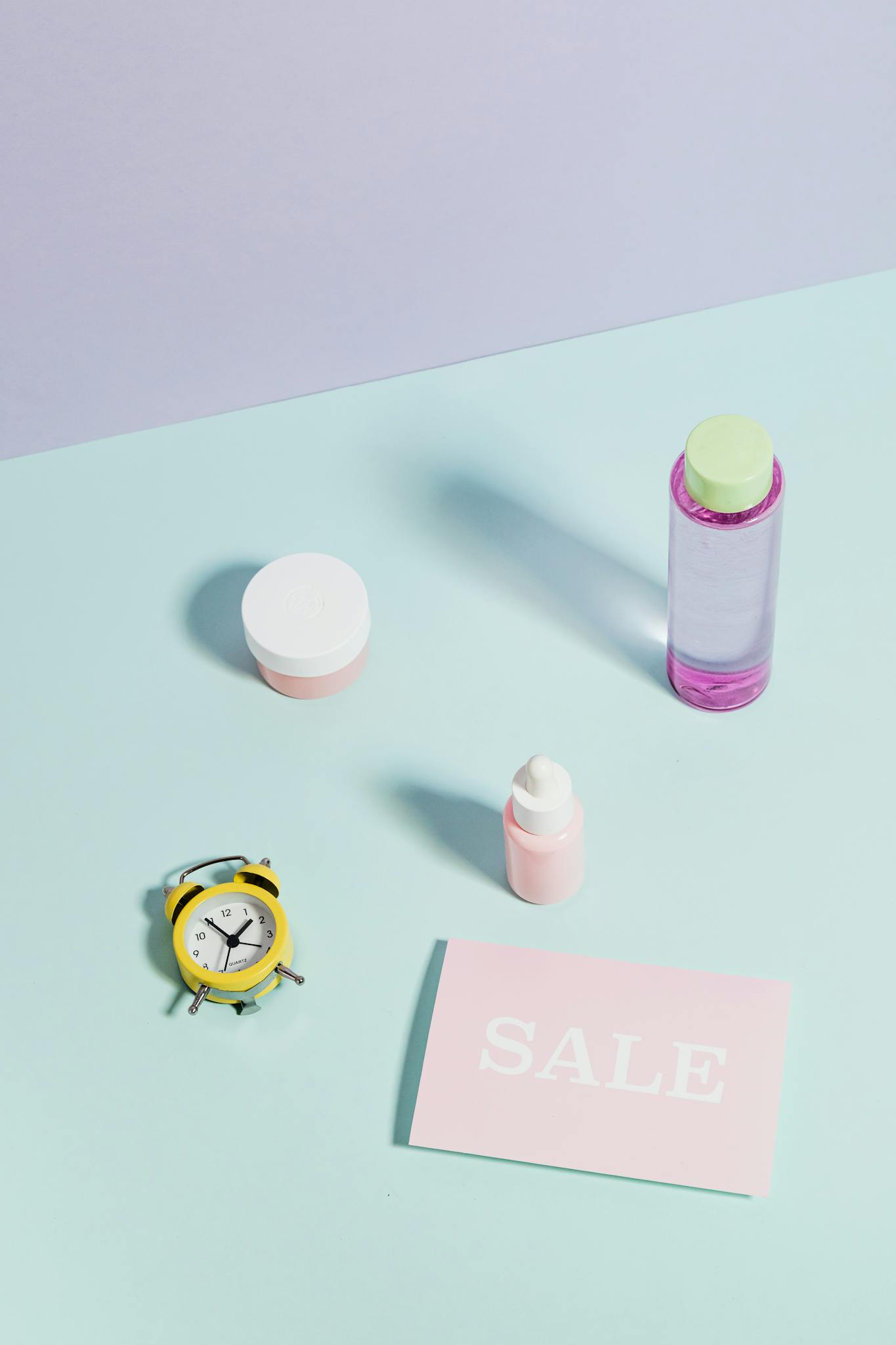 Stylish flat lay of beauty products, alarm clock, and sale card on pastel backdrop.
