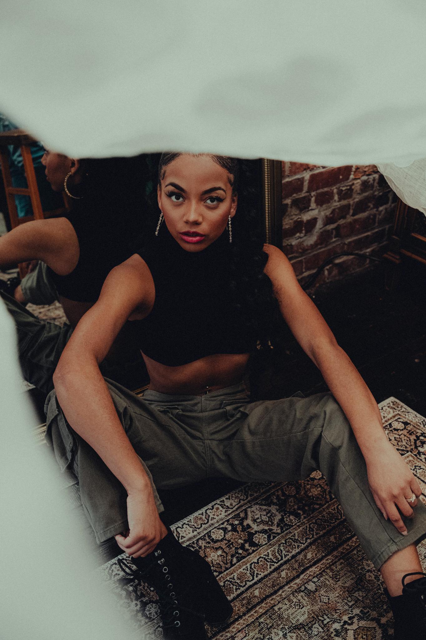 Stylish woman in urban setting, sitting on vintage rug with brick wall backdrop.